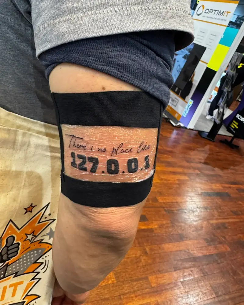 Frisch gestochenes 127.0.0.1-Tattoo am Oberarm, dahinter die Messestände
